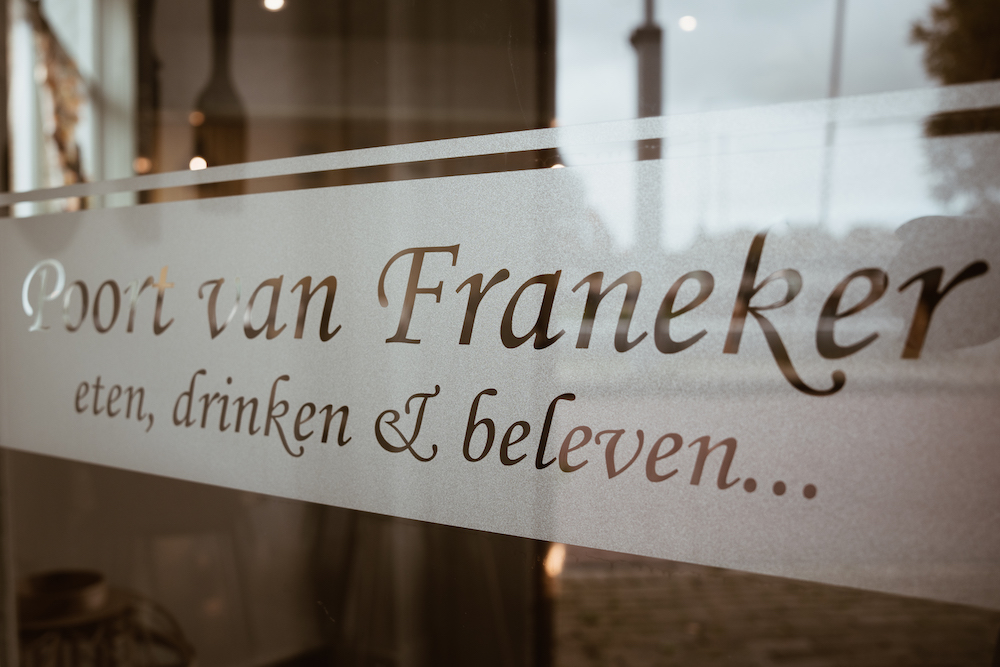 Eten drinken en beleven... slogan van Poort van Franeker op raam hotel-restaurant in Franeker. En op zoek naar een gastvrouw of gastheer.